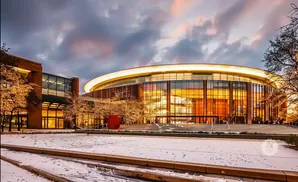 Modern glass arena with a glowing roof, surrounded by illuminated trees, dusted with snow.