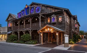 Rustic wooden building with colorful, illuminated windows and a covered entrance at dusk.