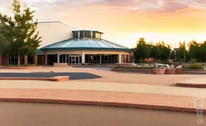 Modern building with a glass rotunda and trees at sunset.