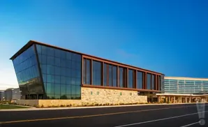 Modern glass and stone building with a copper-colored roof and accents under a clear blue sky.