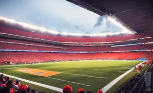 A packed football stadium with fans in red seats and on the field.