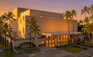 A modern building with palm trees and sunset colors.