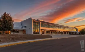 A modern building with a long glass walkway is illuminated by a vibrant sunset sky.