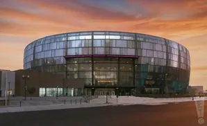 Modern circular building with glass facade at sunset.