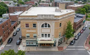 Aerial view of the Somerville Theatre, a yellow brick building with a marquee, surrounded by streets, sidewalks, and other brick buildings.