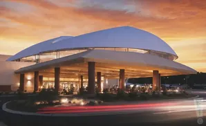 Modern casino entrance with curved roof at sunset, cars blurred in foreground.
