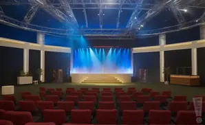 An empty auditorium with red seats facing a brightly lit stage.
