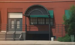Exterior of a red brick building with a semicircular awning over windows and a gray double door.