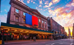 A theater with a marquee illuminated at sunset, under a sky filled with colorful clouds.