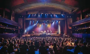 A band performs on a brightly lit stage in a grand theater, facing a large audience.