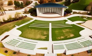An aerial view of an outdoor amphitheater with white seating, a stage, and green lawns.
