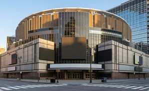 Madison Square Garden, a circular arena with a glass facade, stands under a clear blue sky.