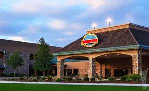 Hotel entrance with stone pillars, a circular sign, and landscaping at dusk.