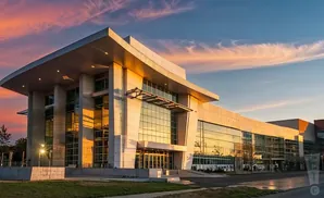 Modern convention center with large glass windows and a curved roof at sunset.