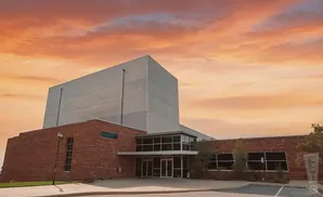 Modern brick building with a large silver facade against a dramatic orange and pink sunset sky.
