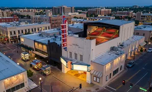 Exterior view of a historic theater with a large marquee and outdoor seating, surrounded by city buildings at dusk.