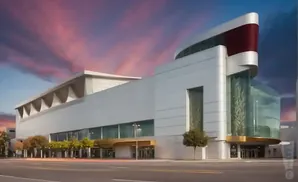 Modern white building with a curved glass entrance and a red accent under a dramatic pink and purple sky.