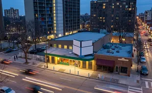 An aerial view of a city street at dusk with light trails from cars and illuminated buildings.