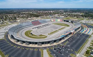 Aerial view of a large oval race track with grandstands and surrounding parking lots and buildings.