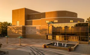 Modern brick building with a glass facade and a fountain plaza, bathed in warm sunset light.