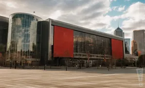 Modern building with a curved glass facade and a large red section under a cloudy sky.