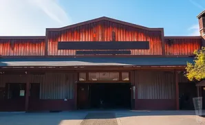 An open barn entrance with red metal siding above and wooden stalls below.