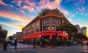 Corner building with neon lights and a colorful sunset sky.
