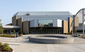 Modern building with large glass entrance and circular concrete seating area in a paved plaza.
