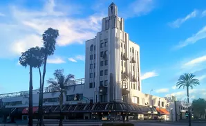 Art Deco skyscraper with tall palm trees in front under a blue sky with clouds.