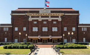 Front view of a large, brick building with an American and Texas flag flying above its entrance.