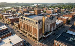 Aerial view of a historic brick theater with ornate details, surrounded by city buildings and a river in the distance.
