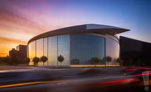 Modern stadium with glass facade at sunset, with light trails from moving cars in the foreground.
