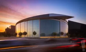 Modern glass arena at sunset with light trails from cars on the road.
