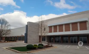 A modern, tan building with large windows and brick accents under a cloudy sky.