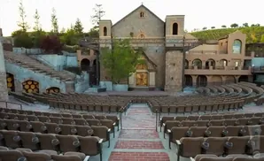 An outdoor amphitheater with stone church facade and vineyard backdrop.