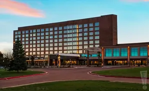 A modern hotel with a brick facade and large windows, lit up at dusk with a colorful sky.