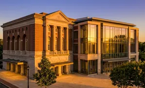 A modern building with classical and glass sections reflects golden sunset light.