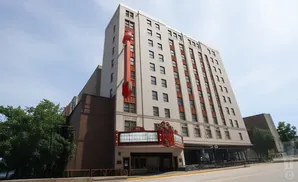 Exterior of a tall, light-colored building with a vintage marquee and a tall red sign hanging down the side.