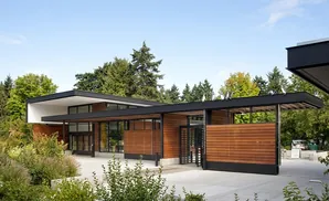 Modern wooden building with black roof, surrounded by trees, and penguins on the roof.