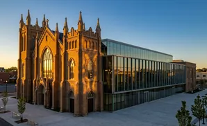 Modern glass addition complements historic brick church at sunset.