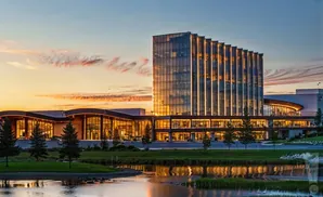 Modern glass building with illuminated windows at sunset, reflected in a calm body of water.
