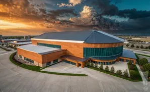 An aerial view of a modern building with wood and glass facades, set against a dramatic sunset sky.