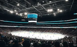 An ice hockey game is being played in a packed arena with a large scoreboard hanging above the ice.