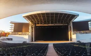 An outdoor amphitheater with rows of empty seats facing a large stage under a white canopy.