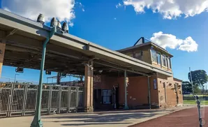 A brick building with a metal roof and gates under a bright blue sky with clouds.