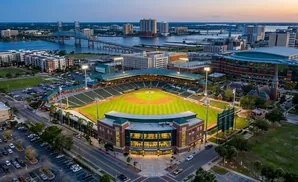 Aerial view of a baseball stadium at dusk with city skyline and a bridge in the background.