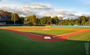 A baseball field with manicured grass and clay baselines under a partly cloudy sky.