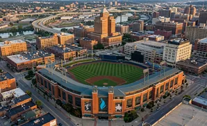 Aerial view of a baseball stadium in a city with buildings and a highway.