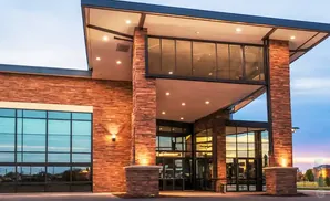 Modern stone-clad building with large glass windows and an overhang at dusk.