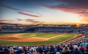 Baseball stadium at sunset with players on field and spectators in the stands.